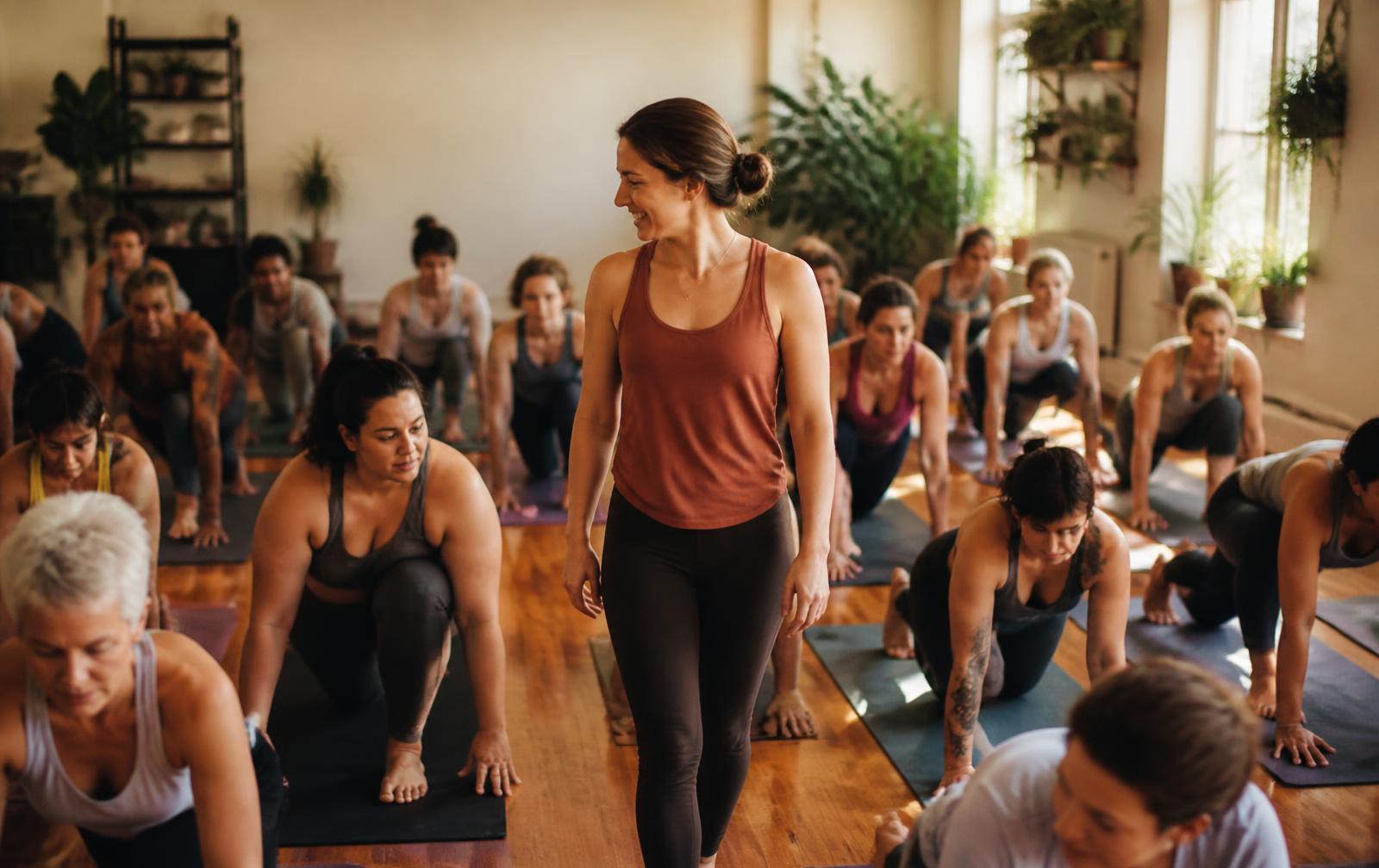 A full paid class in a sunlit studio, the instructor walking between rows