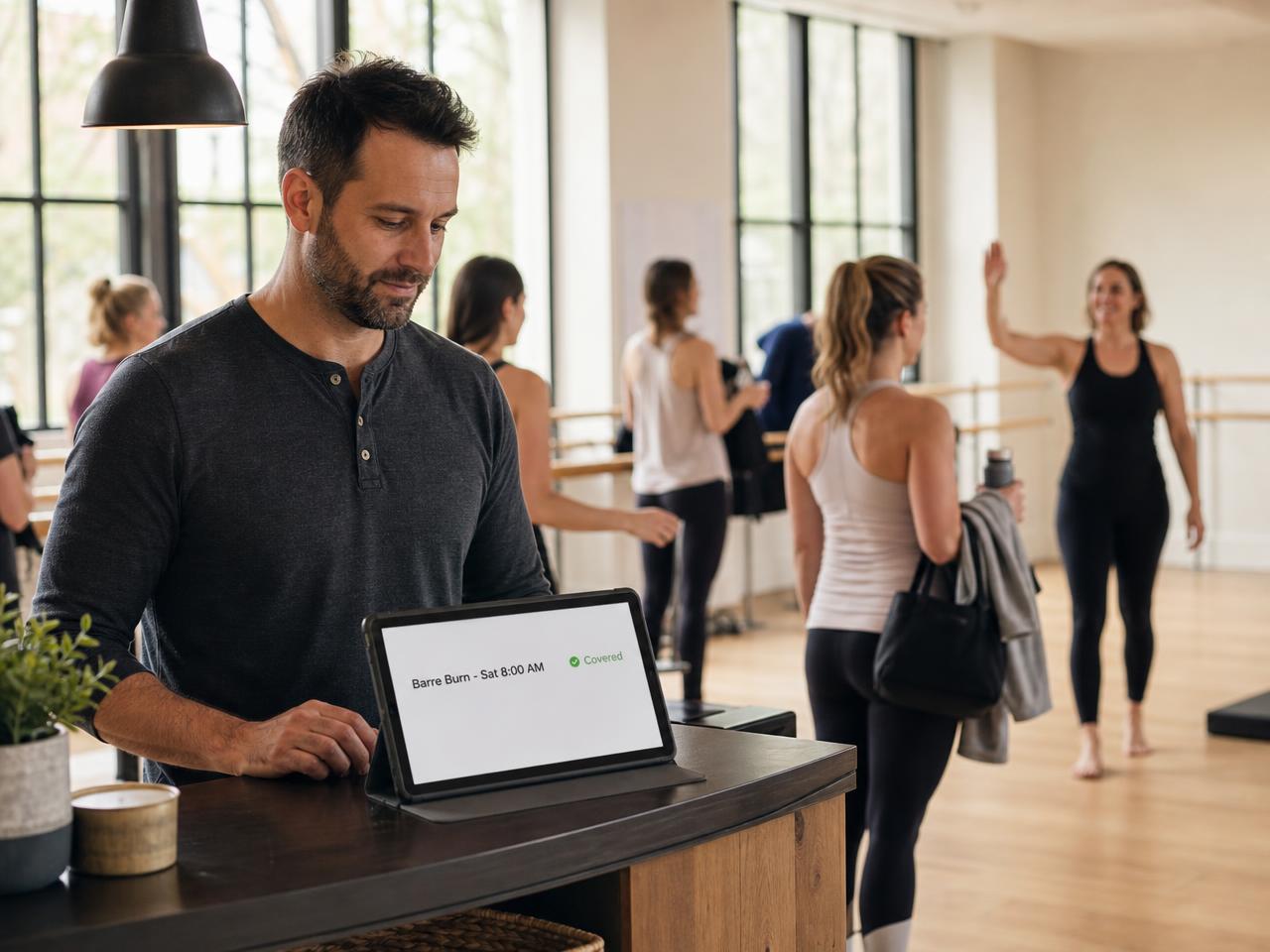 A studio manager approving a substitute instructor on a tablet at the front desk